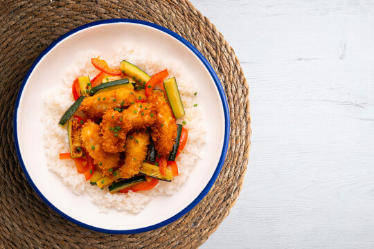 Battered chicken strips with vegetables and a white rice base. Overhead view of the table.