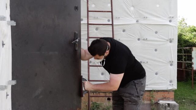 male homeowner sanding severe corrosion from an aging exterior steel door, carrying out diy surface preparation before repainting and residential property repair