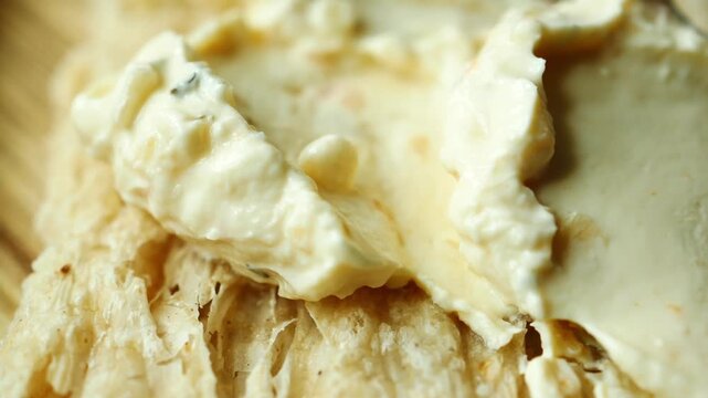 Macro close up of white cream cheese spread on flaky toasted pastry appetizer showing smooth texture and light reflections