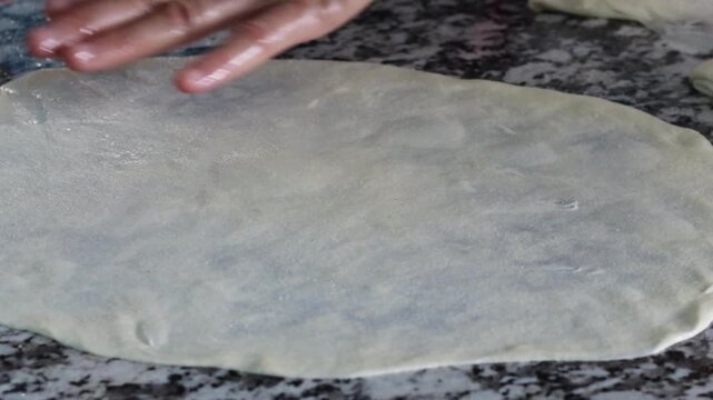 Hands stretching and folding msemen dough on marble counter