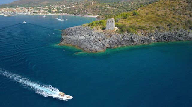 Marina di Camerota Cilento Italy 4K drone video. Torre del Zancale watchtower pivot revealing bay with fast rental speed boat and white wake. Punta Infreschi hidden caves. Dynamic coastal travel 