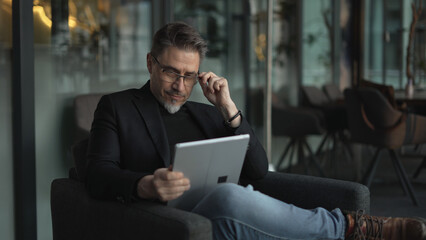 Businessman using tablet computer in office. Middle aged man in business casual, Entrepreneur working online, reading finance report, thinking.  . © nyul