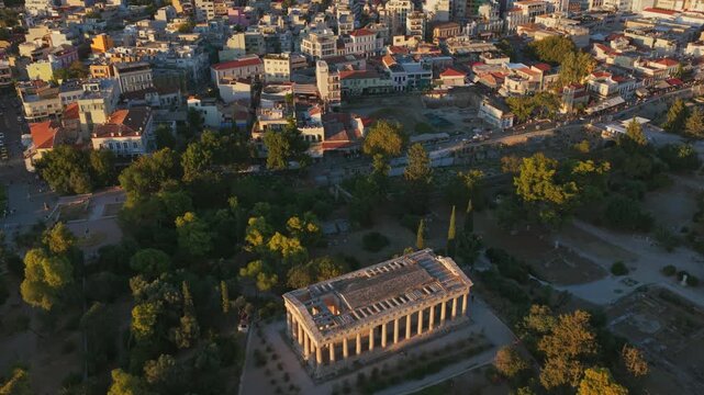 Glorious aerial view showing the Temple of Hephaestus within the ancient Agora of Athens, slowly revealing the magnificent cityscape of Greece's capital and Lycabettus Hill in the background