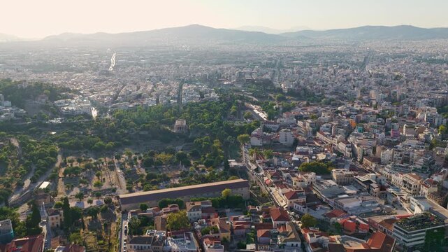 Aerial view flying over the historic ancient Agora of Athens in Greece, revealing the famous Temple of Hephaestus and the Stoa of Attalos with the sprawling cityscape in the background