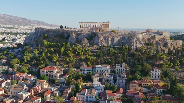 Breathtaking aerial footage flying around the iconic Acropolis, revealing the ancient Parthenon temple and the historic Plaka district with the sprawling city of Athens in the background