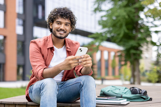 Smiling student drinking takeaway coffee and using smartphone during study break on campus grounds.