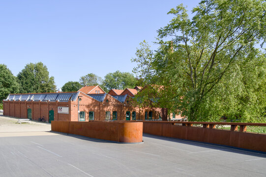 Historic brick textile factory building with sawtooth roof and modern rusty steel bridge in Bocholt