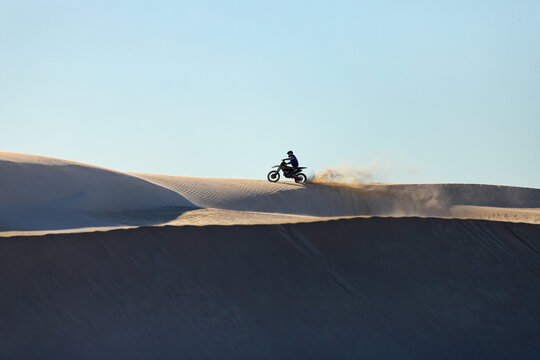 View of a person riding a dirt bike across the Lancelin Sand Dunes, kicking up sand in the bright sunlight, Lancelin, Western Australia, Australia.
