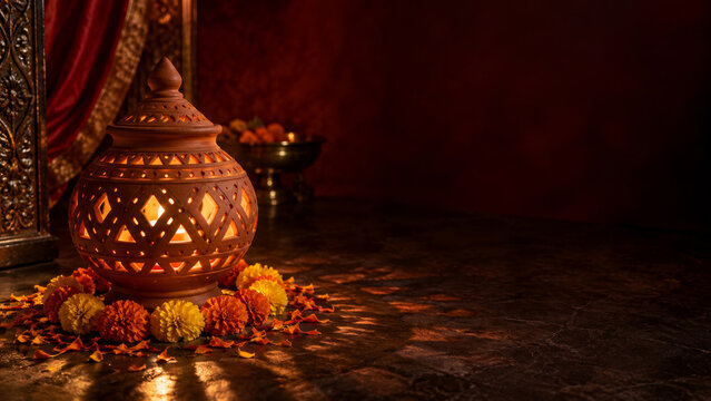 Glowing clay lantern with burning candle surrounded by marigold flowers on dark floor. Traditional Indian decoration for Navratri festival celebration.