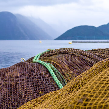 View of fish farm nets piled on a dock with a fjord and mountains in the background in Stranda, More og Romsdal, Norway.