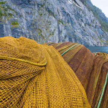 View of fish farm nets piled up against a steep rocky cliff face in the fjord at Stranda, More og Romsdal, Norway.