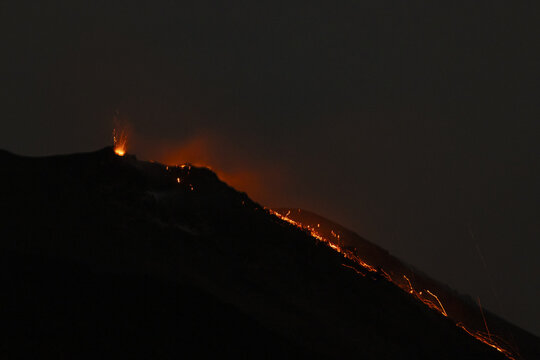 View of Stromboli erupting at night with glowing lava flowing down the dark volcanic slope, Lipari, Sicilia, Italy.