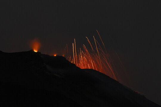 View of Stromboli volcano erupting at night with glowing lava and sparks against a dark sky in Lipari, Sicilia, Italy.