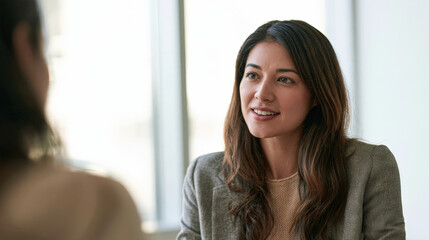 Fototapeta premium An authentic portrait captures an Asian businesswoman, wearing a high-end textured grey wool blazer, in a meaningful conversation with a colleague within a modern, light-filled office space.