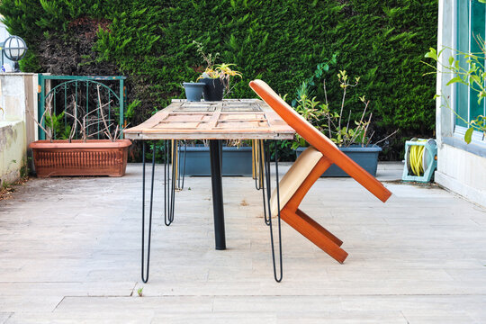 Urban street scene with wooden chair balanced on two legs leaning against table, unusual outdoor furniture arrangement in city.