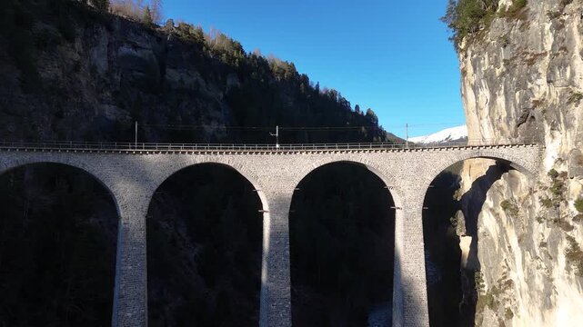 landwasser viaduct spans forested gorge near filisur switzerland six limestone arches curve across ravine railway line meets sheer rock cliff aerial drone footage blue sky mountain scenery graubunden