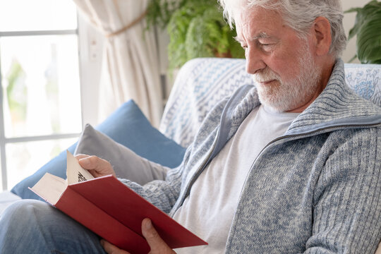 Senior man enjoying leisure time at home, relaxing on a comfortable sofa while deeply engrossed in reading a book, finding peace and quiet during retirement
