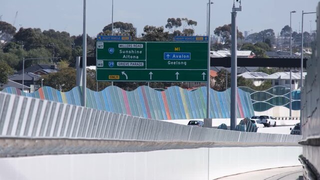 View of directional road signage at West Gate Freeway from an adjacent shared path, displaying routes to Sunshine, Altona, Avalon, Geelong, with busy traffic and&nbsp;sound barriers in Melbourne Australia