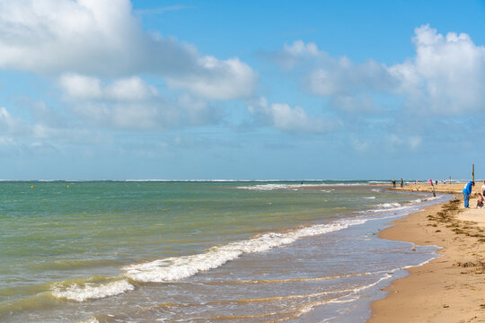 View of the sandy beach at Aberdyfi with gentle waves, people walking along the coastline, and a bright blue sky with scattered clouds in Aberdyfi, Wales, United Kingdom.