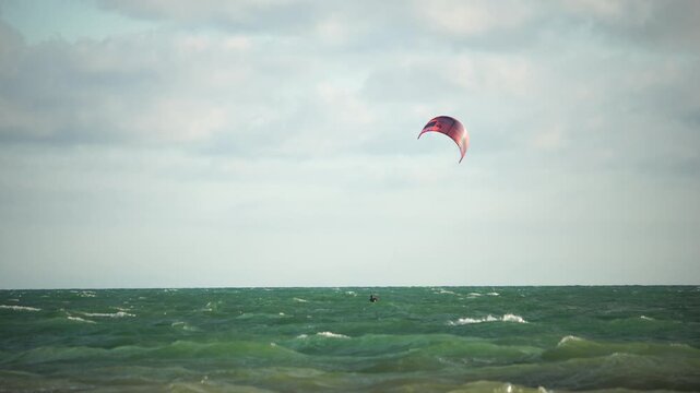 Kiteboarding, Beach, Ocean - Red Kite Soaring Over Choppy Water on a Cloudy Day.