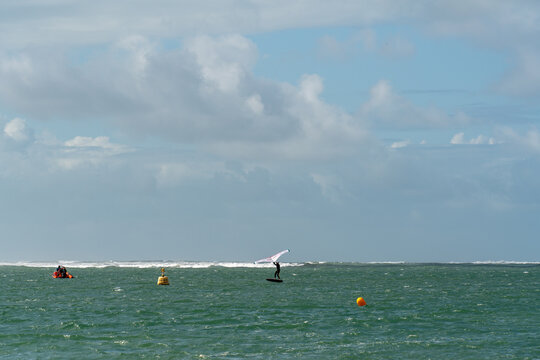 View of a person wing foiling on the sea with a small boat and buoys in the water under a cloudy sky in Aberdyfi, Wales, United Kingdom.
