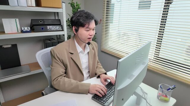 Young asian professional customer service agent working on computer in office, using headset to communicate with customer