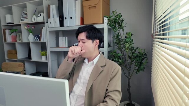 Exhausted businessman working alone at an office computer, feeling sleepy and fatigued while forcing himself to continue working and finish his tasks.