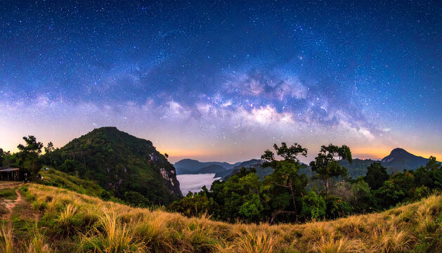 グラデーションの夕空から星空へと移り変わる山並みと草原の夜景写真素材