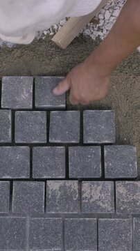 Vertical top down view of a builder installing gray paving stones with a rubber mallet