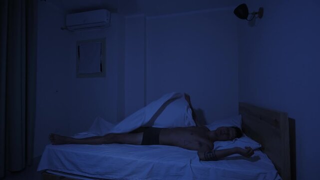 Man struggling to get comfortable on sleepless hot night, repeatedly changing position and throwing off covers because of extreme heat