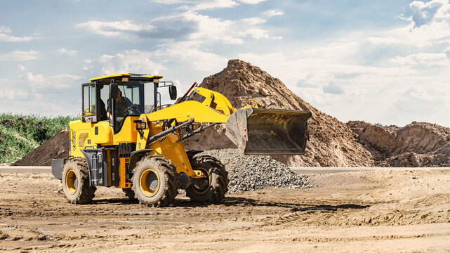 A loader is moving dirt at a landscaping site. The loader lifts material while a pile of dirt is visible nearby. The ground is clear and prepared for work