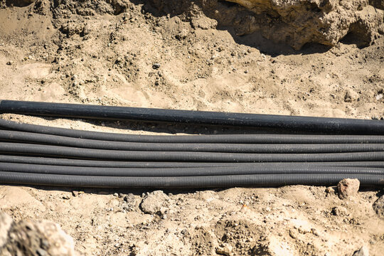Several black cables are laid in a trench filled with soil and dirt. The cables are arranged neatly along the base of the trench