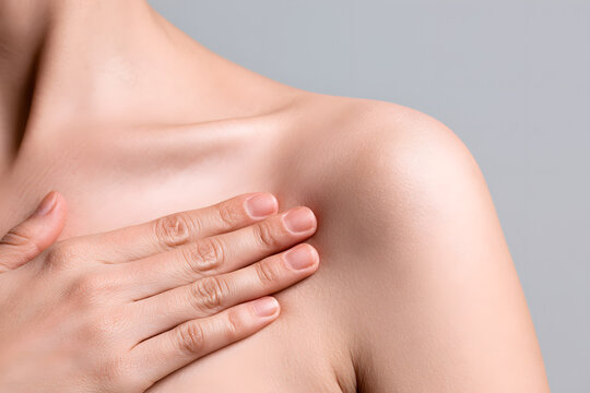 A woman is conducting a breast examination, palpating lumps for indications of breast cancer, against a gray backdrop. The image conveys a healthcare theme.