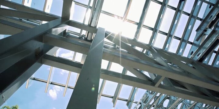 Sunlight beams penetrate through the open metal structural framework of a new commercial building construction site highlighting the raw industrial engineering design elements for architectural