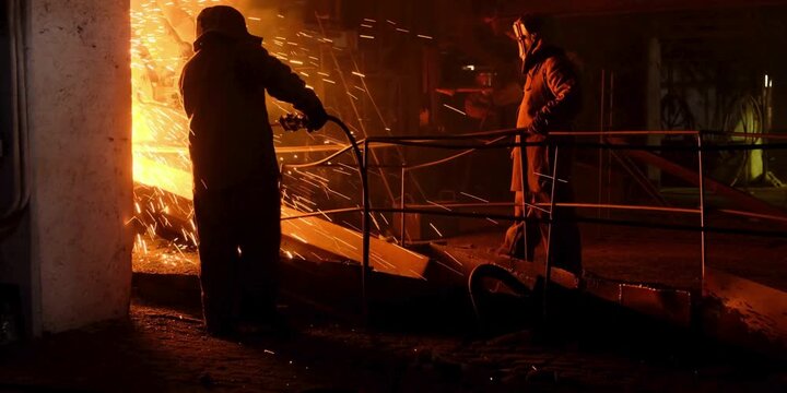 Industrial metal workers manage molten liquid flow inside a heavy factory smelting furnace creating sparks while wearing protective gear during the intense manufacturing process for raw steel