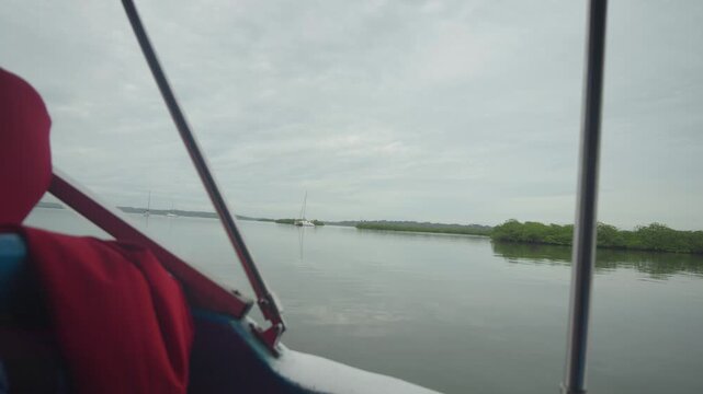 Interior of a boat shows red life jacket. Calm water stretches toward distant greenery. Overcast sky frames serene waters. Ideal for tranquil water travel projects