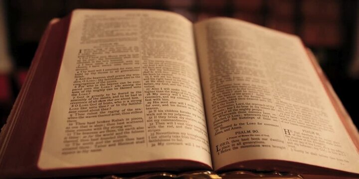 An open antique religious scripture with weathered pages rests on a wooden surface representing deep spiritual contemplation while soft warm light illuminates the sacred text for quiet peaceful
