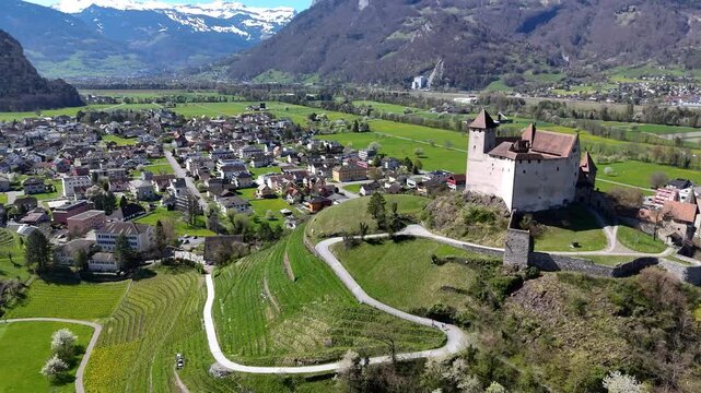 switchback path terraced hillside vineyard slopes gutenberg castle round tower hilltop balzers town rooftops snowcapped alpine peaks farmland rhine valley liechtenstein drone footage aerial view