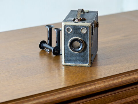 An antique box camera and film spools rest on a wooden surface, evoking a sense of nostalgia for classic photography and analog art.