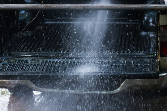 Water spray cleaning dark pickup truck cargo bed with textured liner, creating dramatic outdoor vehicle maintenance scene and visible splash pattern
