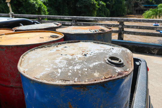 Weathered metal drum with rust, peeling paint, and industrial containers outdoors