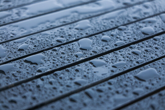 Wet dark wooden surface covered with rain droplets and beads, creating cool blue textured background with parallel lines and reflective moisture