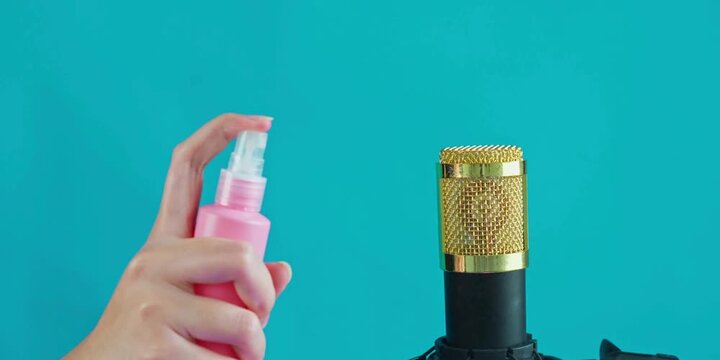 A person sanitizing a professional recording microphone using a pink bottle spray to ensure hygiene and cleanliness during podcast production sessions for high quality audio broadcasts in the