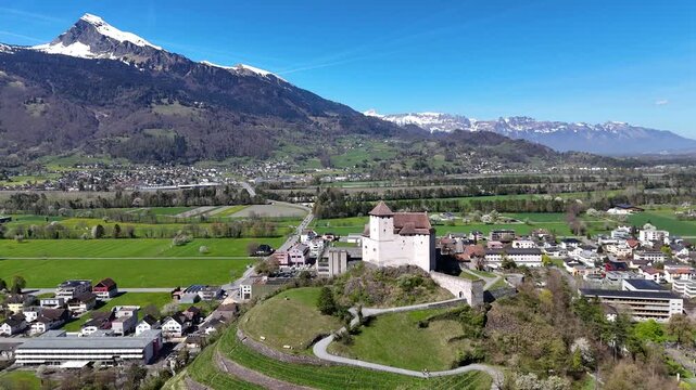 towering snowcapped peak backdrop rhine valley gutenberg castle round tower parish church spire balzers town rooftops modern office buildings farmland liechtenstein drone footage panorama clear sky