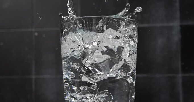 Ice cubes falling into a glass of water with splash in slow motion