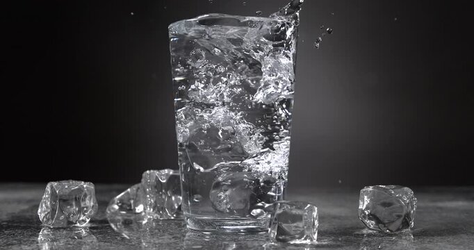 Ice cubes falling into a glass of water with splash in slow motion