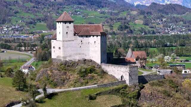 round tower pyramidal roof gutenberg castle white walls gatehouse defensive walls rocky outcrop hilltop parish church valley farmland liechtenstein balzers drone footage aerial view heritage site