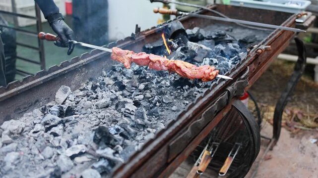 Cook in black gloves placing skewer with raw marinated meat on charcoal grill. Barbecue shashlik cooking over hot coals with smoke. Outdoor grilling concept.