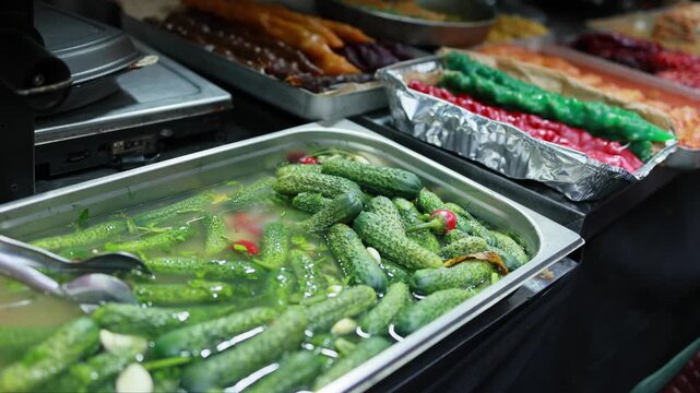 Pickled cucumbers with spices in metal tray at street food market stall. Traditional fermented vegetables with chili pepper and garlic among oriental dishes for sale