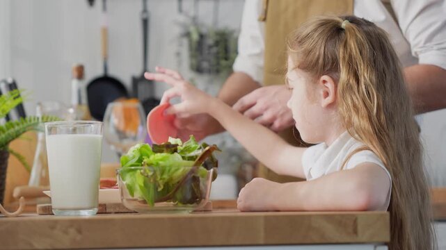 Happy young girl helping father cook meal at home, Father and daughter preparing healthy food together in modern kitchen, Family time cooking concept with dad and daughter in domestic kitchen
